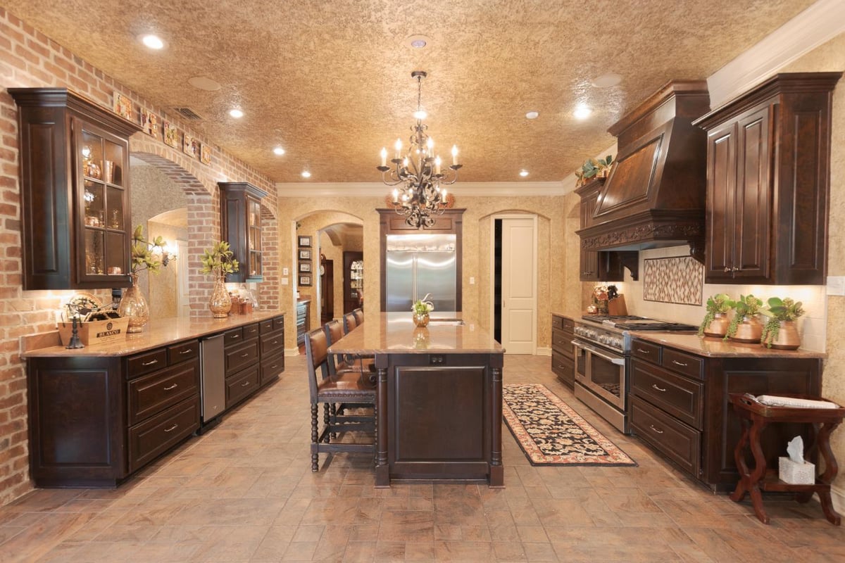 Country French custom home kitchen by Bort Design featuring dark wood cabinetry, brick accents, and a large island in Longview, -optimized