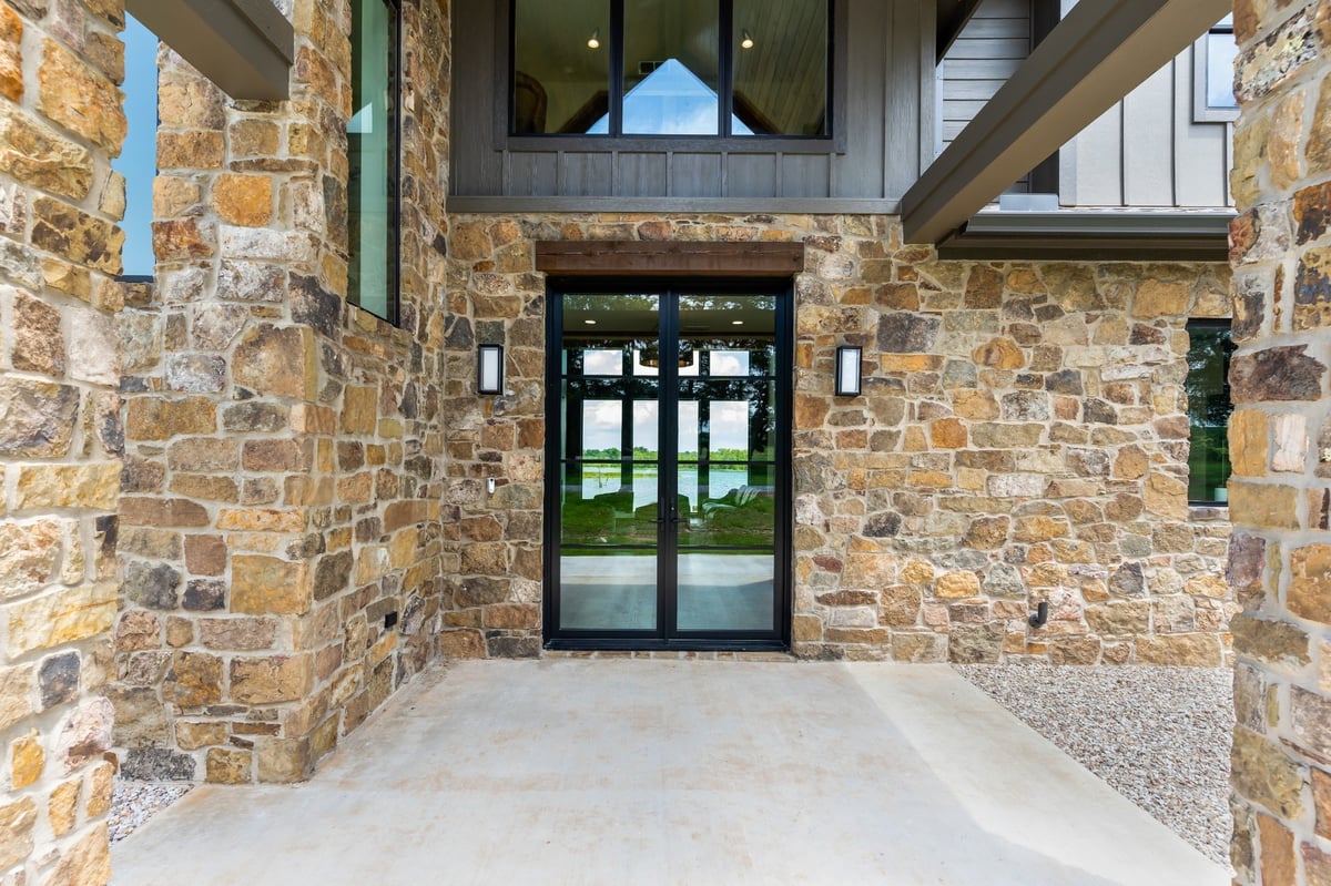 covered entry courtyard with stone walls and glass doors in longview texas custom home
