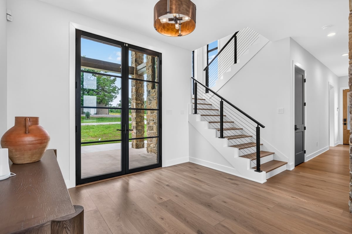 modern foyer with black framed glass doors and floating staircase in longview texas custom home