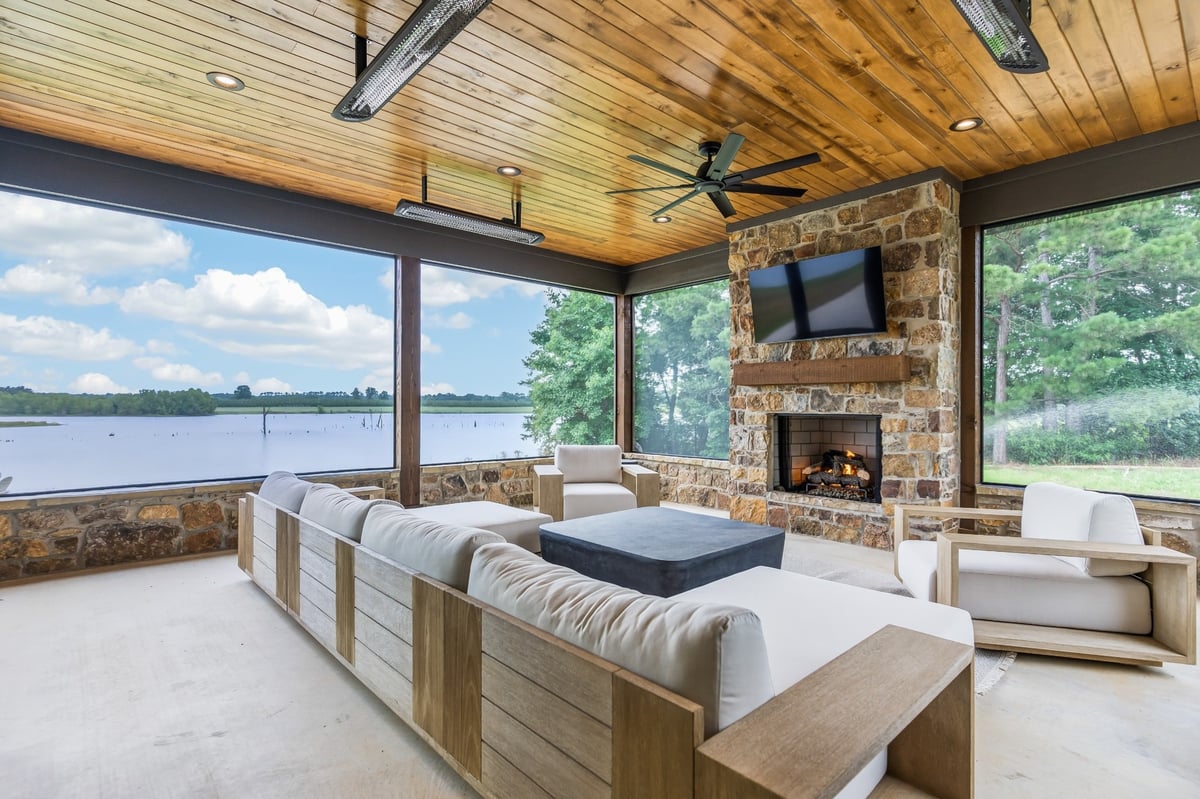 screened outdoor living room with stone fireplace and lake view in longview texas custom home