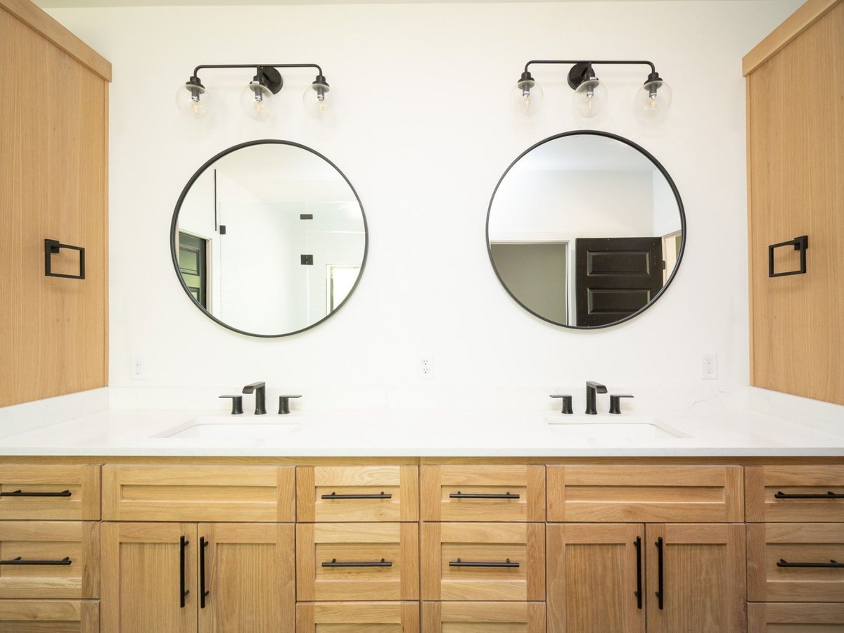 Photo of a double vanity with natural wood cabinets, round mirrors, and black fixtures in an East Texas bathroom.