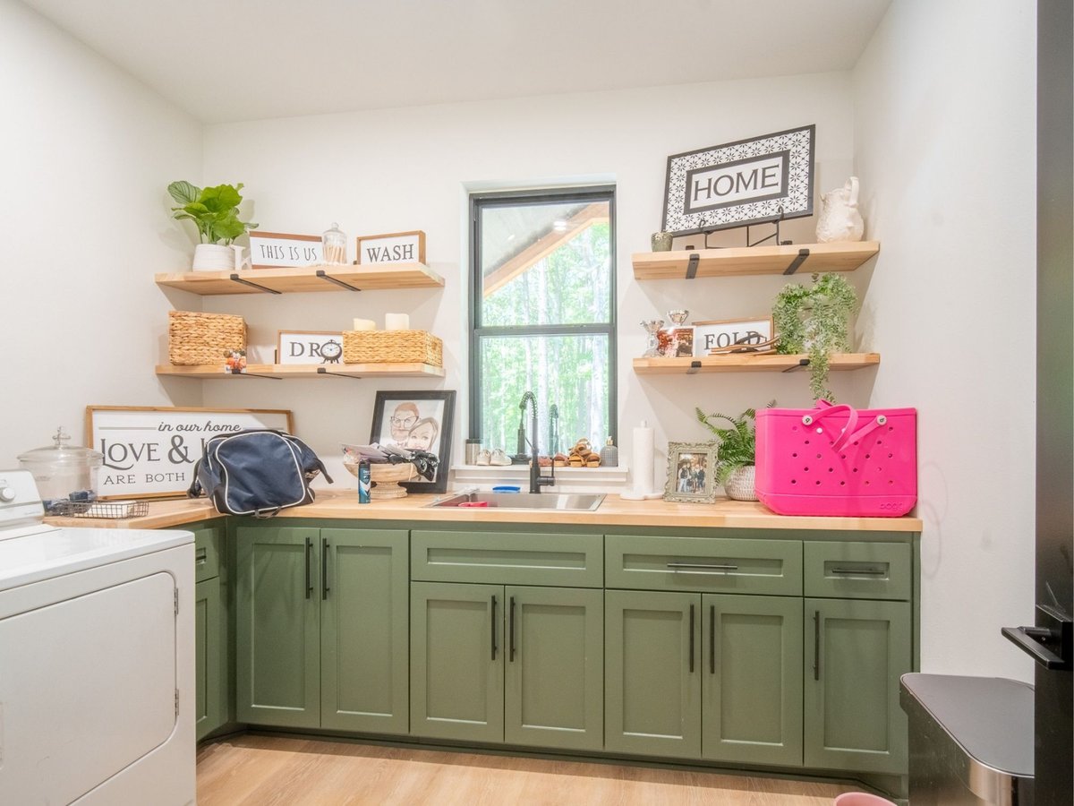 Photo of a laundry room with green cabinets, wood countertops, open shelving, and utility sink in East Texas.