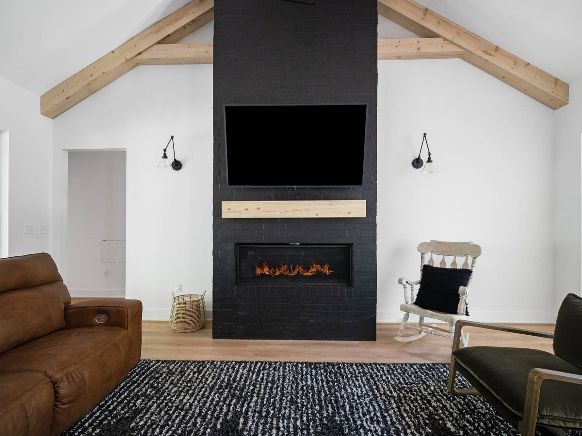 Photo of a living room with exposed wood beams, black brick fireplace, and vaulted ceiling in East Texas.