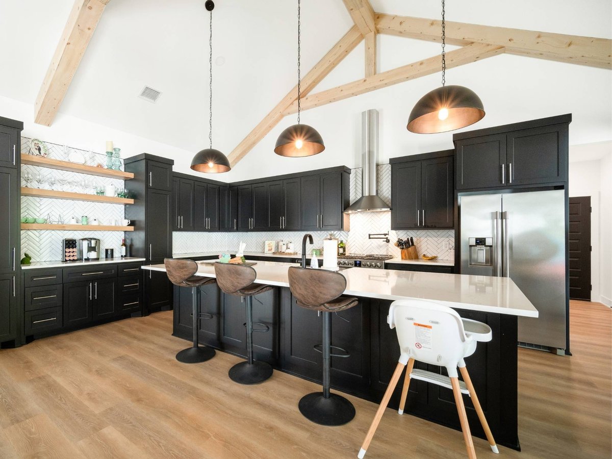 Photo of a modern kitchen with black cabinets, large island, wood beams, and pendant lights in East Texas.