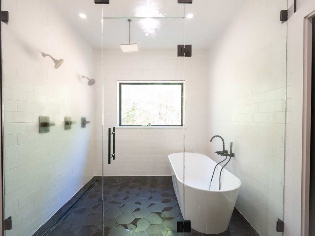 Photo of a walk-in shower with white tile, black hexagon flooring, and freestanding tub in an East Texas bathroom.