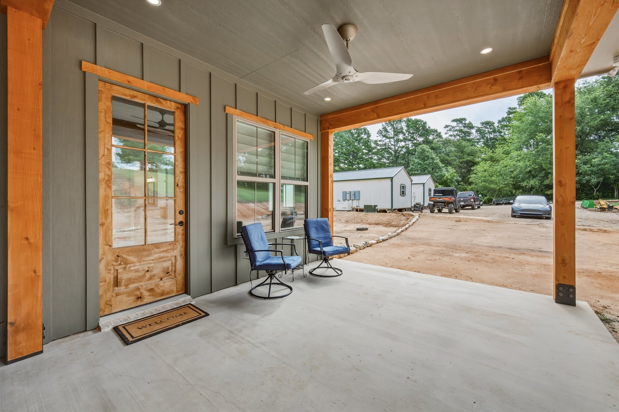 Covered porch of a Bort Custom Homes residence in Henderson, TX, with timber posts, gray siding, and a wood-framed glass door.