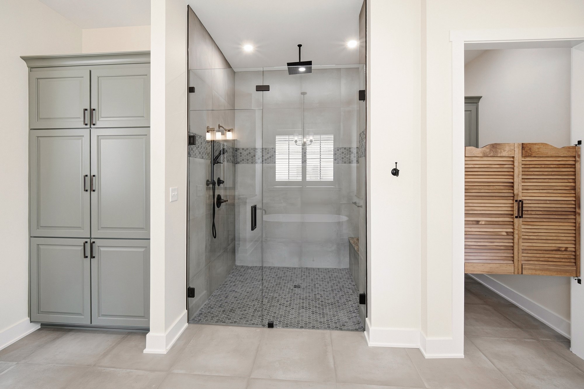 Glass-enclosed shower beside louvered saloon doors in a Henderson, TX bathroom by Bort Custom Homes.