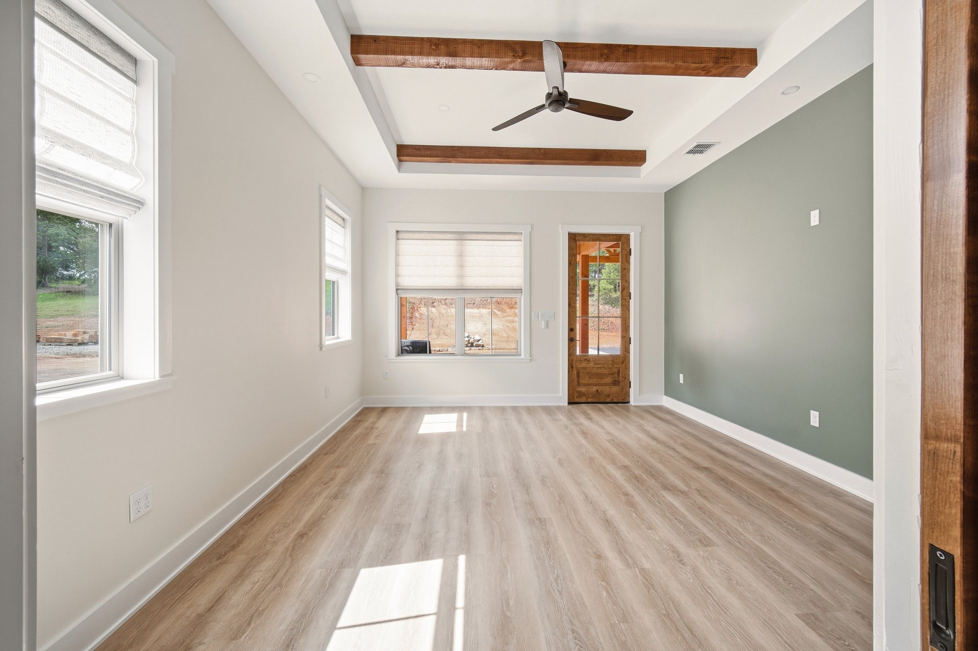 Sunlit room in a Bort Custom Homes residence in Henderson, TX, with stained ceiling beams, a sage accent wall, and a wood door to the porch.